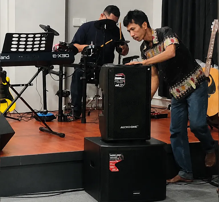 Proses setting dan tuning speaker Audio One professional sound system di sekolah musik modern untuk kebutuhan latihan band, vocal, dan performing arts indoor.